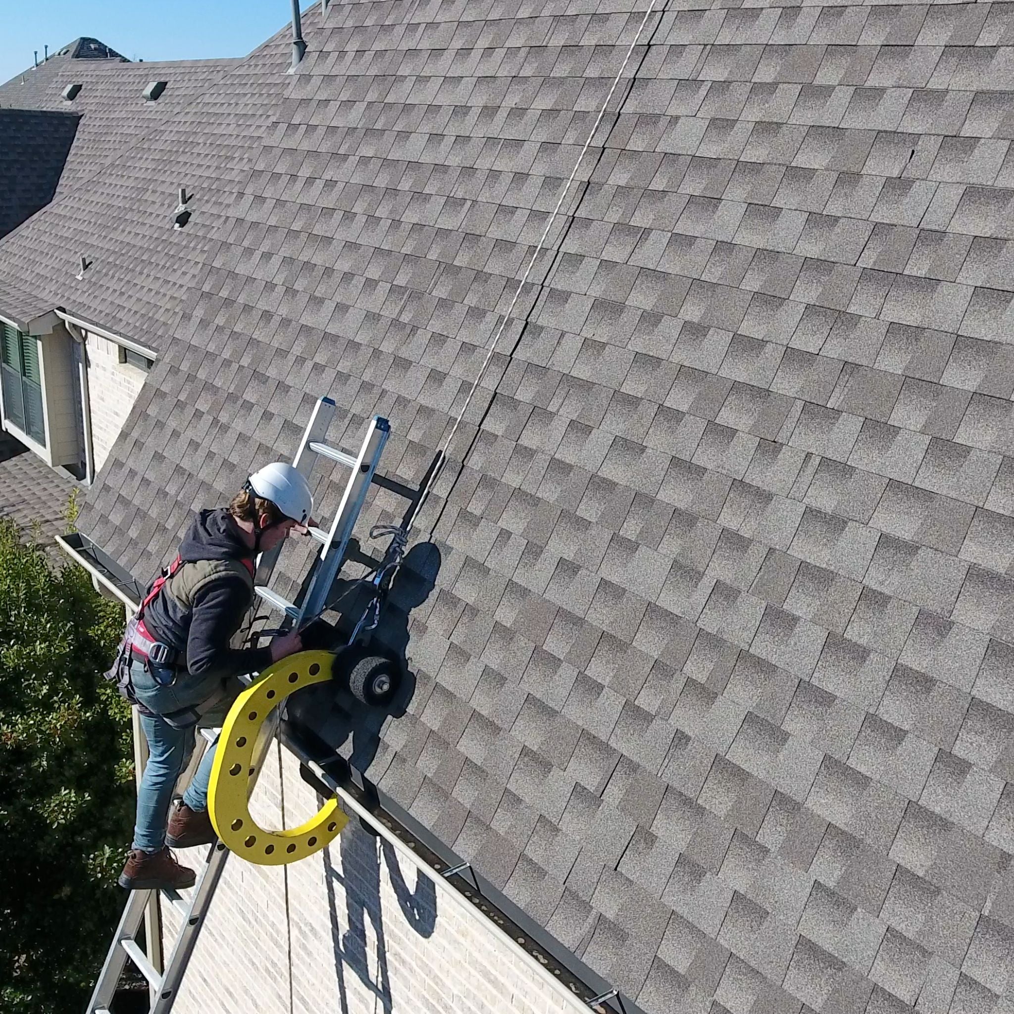 Roof worker climbing to the top of the ladder wearing PPE roof safety harness and white CAMP Safety helmet next to the Eveook Fall Protection System on a very steep slope roof.