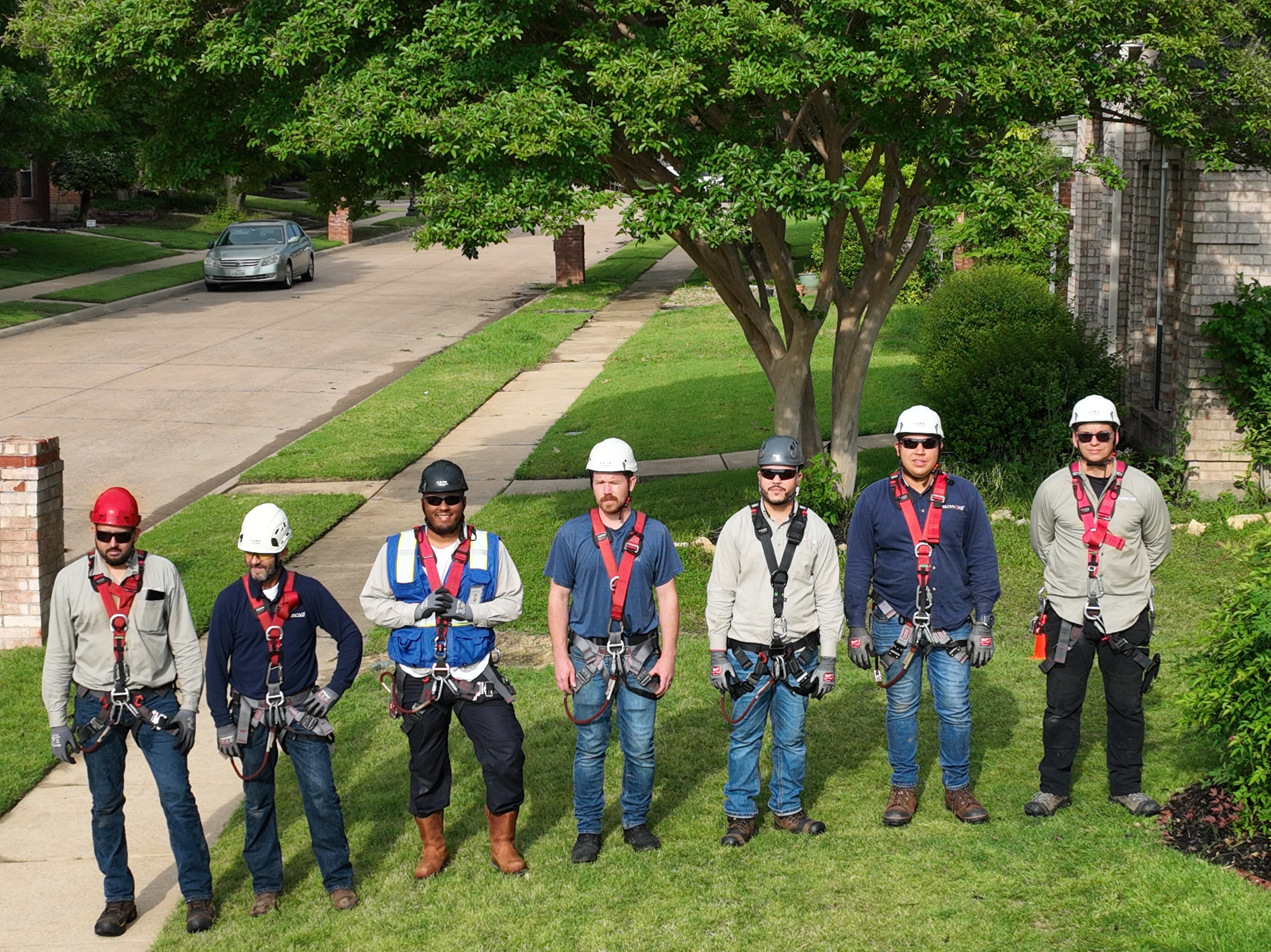 Group of roof workers all wearing PPE, roof helmets, and roof safety harnesses standing in a line.