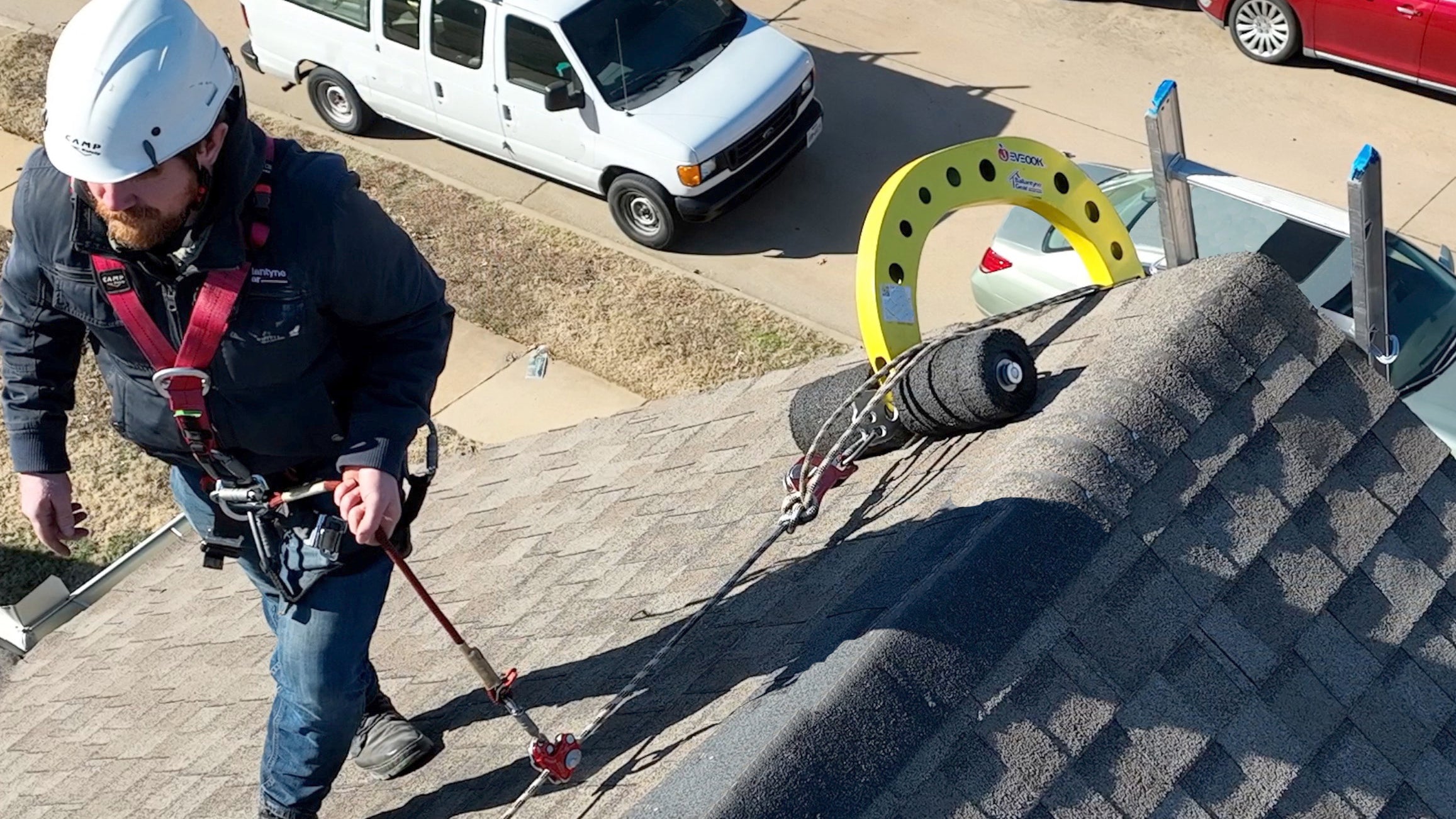 Roof worker using Eveook gable to gable installation for sloped roof fall protection on residential roof wearing roof helmet and PPE.