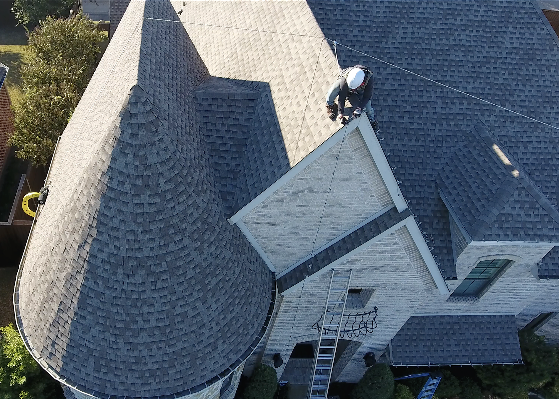 Person working on the edge of a steep roof with a ladder and Eveook Fall Protection System, surrounded by trees and a house.
