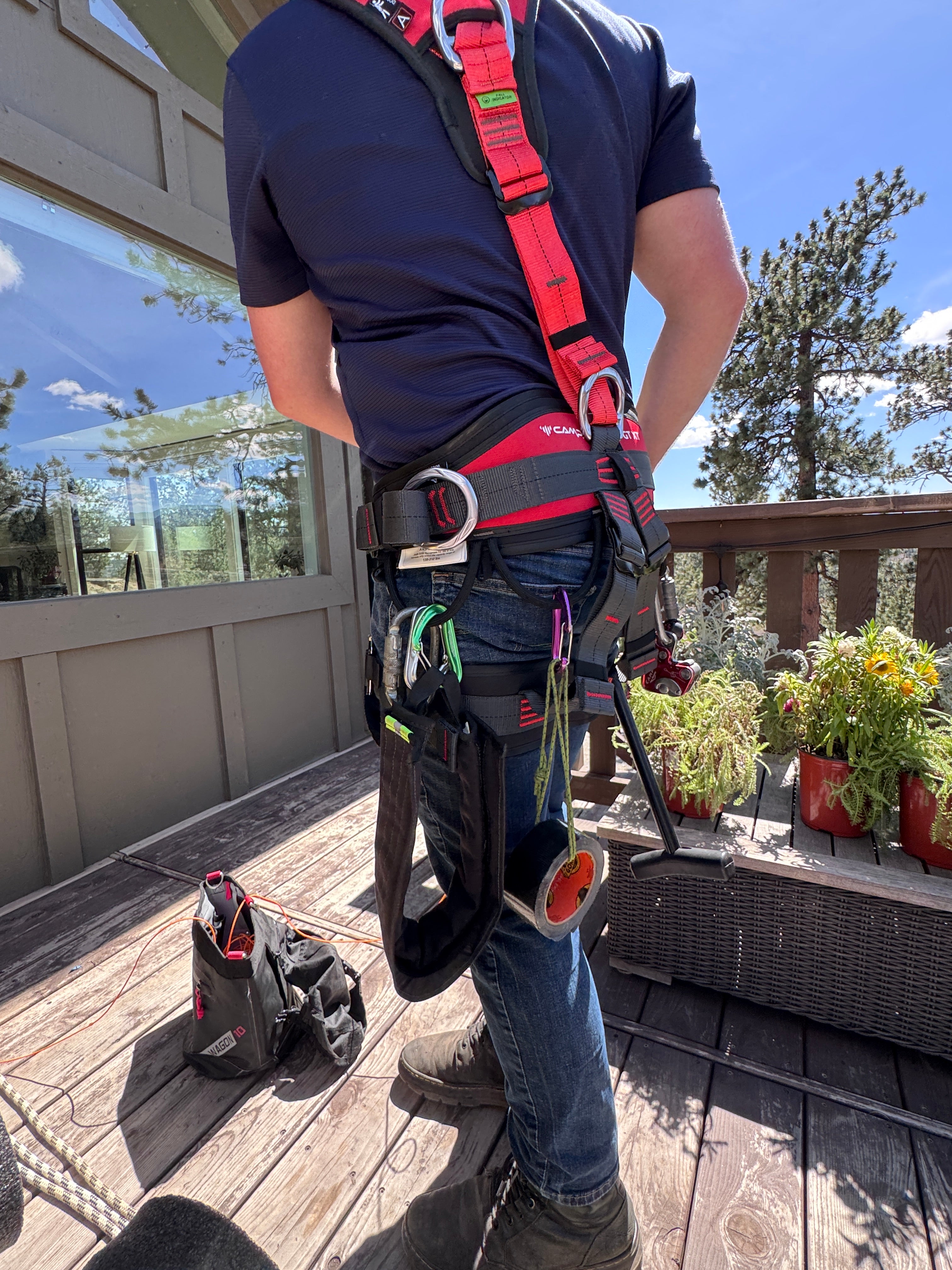 Person wearing a red and black roof safety harness with accessories on a wooden deck
