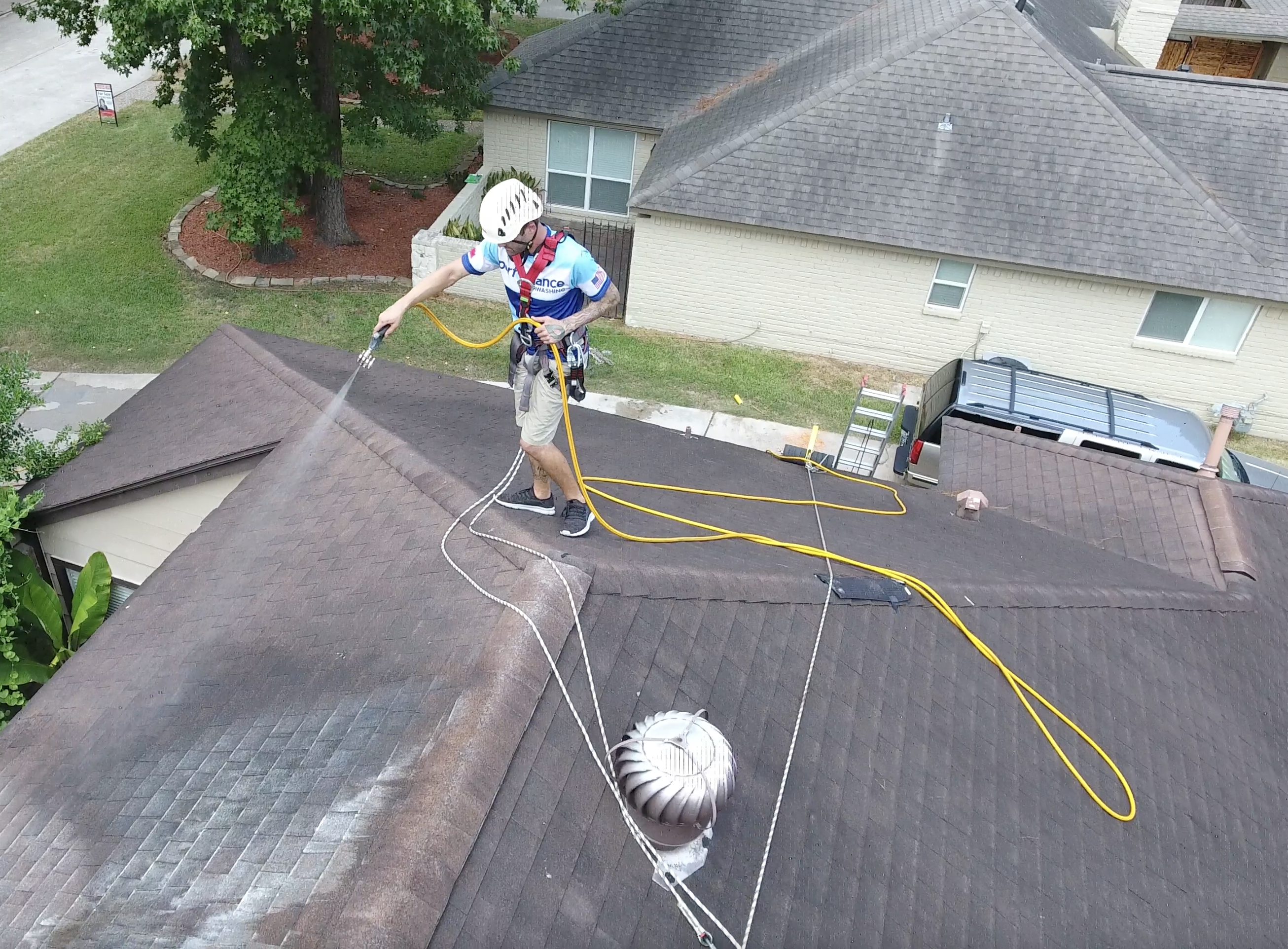 A roof cleaner wearing fall protection and PPE on a sloped roof while spraying chemicals and using the Eveook Fall Protection Sytem.