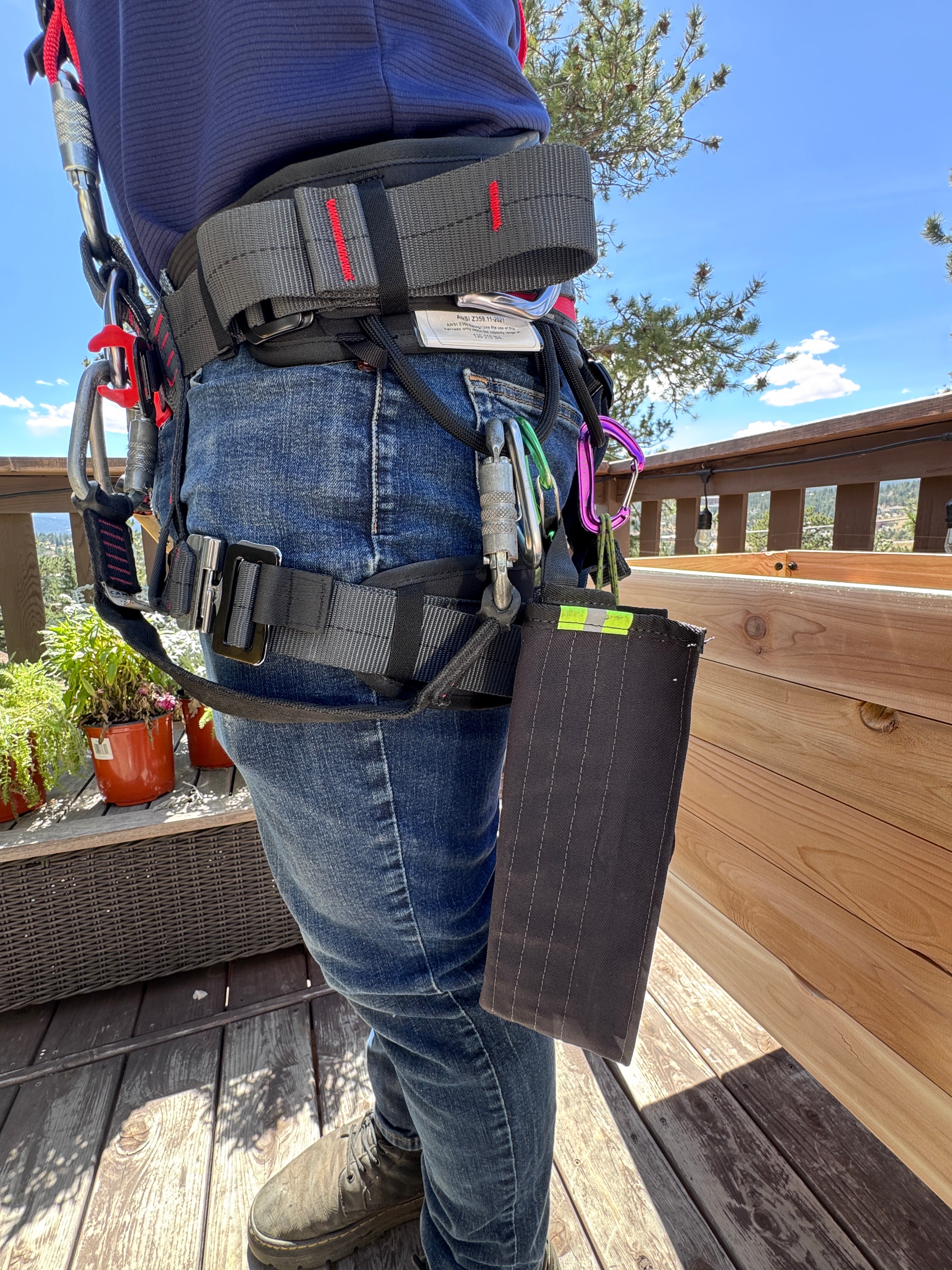 Person wearing a roof safety harness on a wooden deck with a clear blue sky.