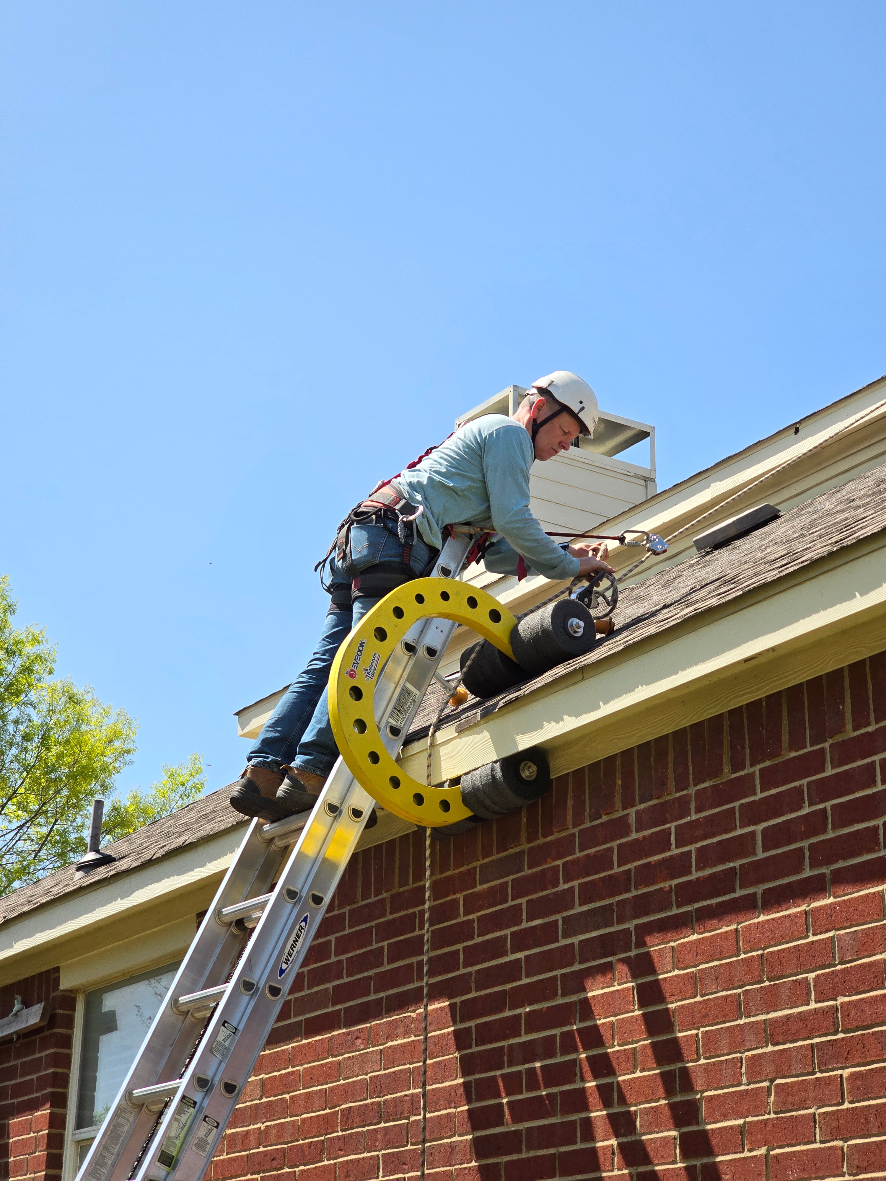 Roof worker at edge of roof at the top of a ladder connecting into his Eveook Fall Protection System wearing an ANSI CAMP safety helmet and roofing PPE