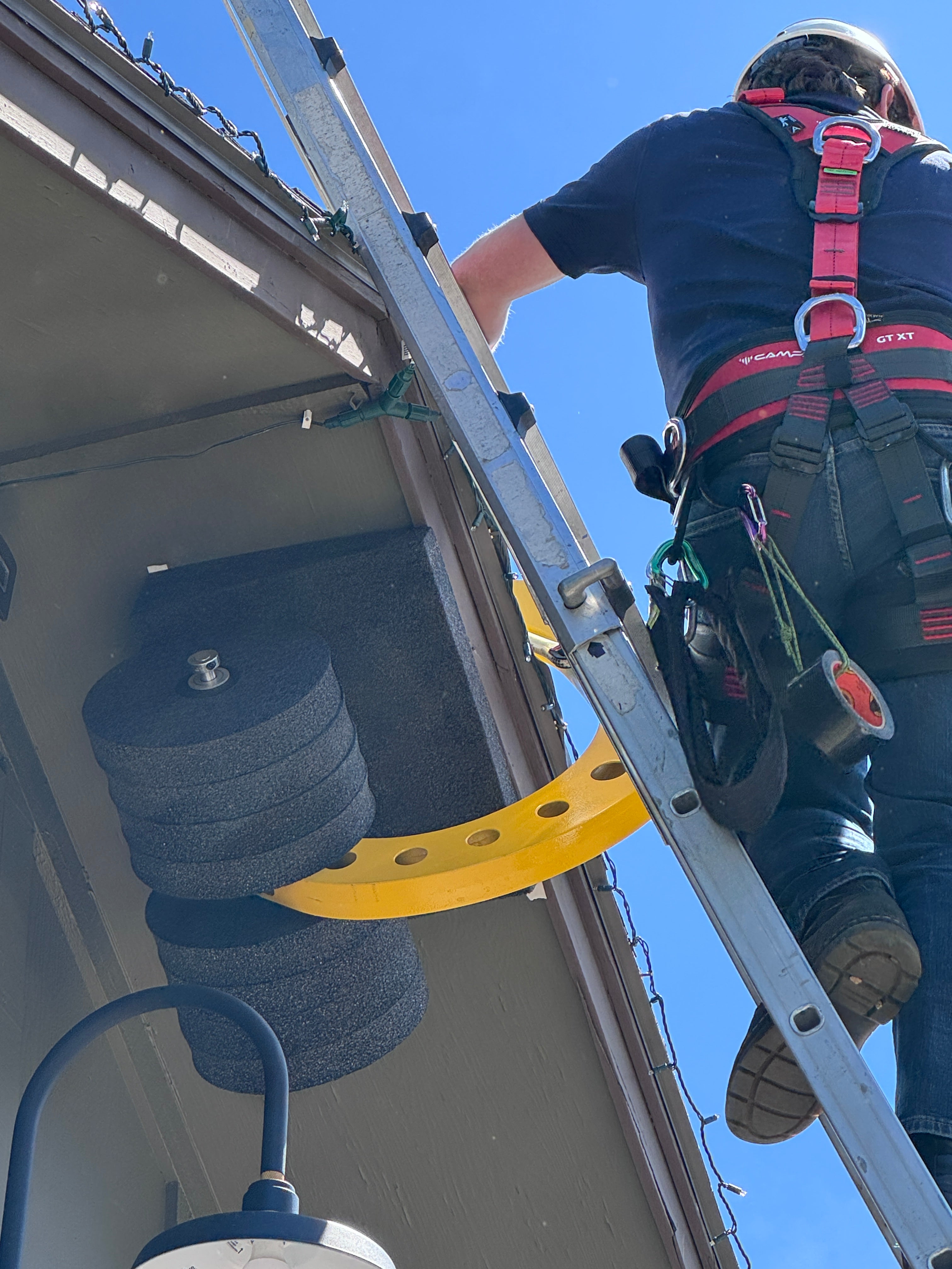 Person on a ladder working on a roof with a clear blue sky background