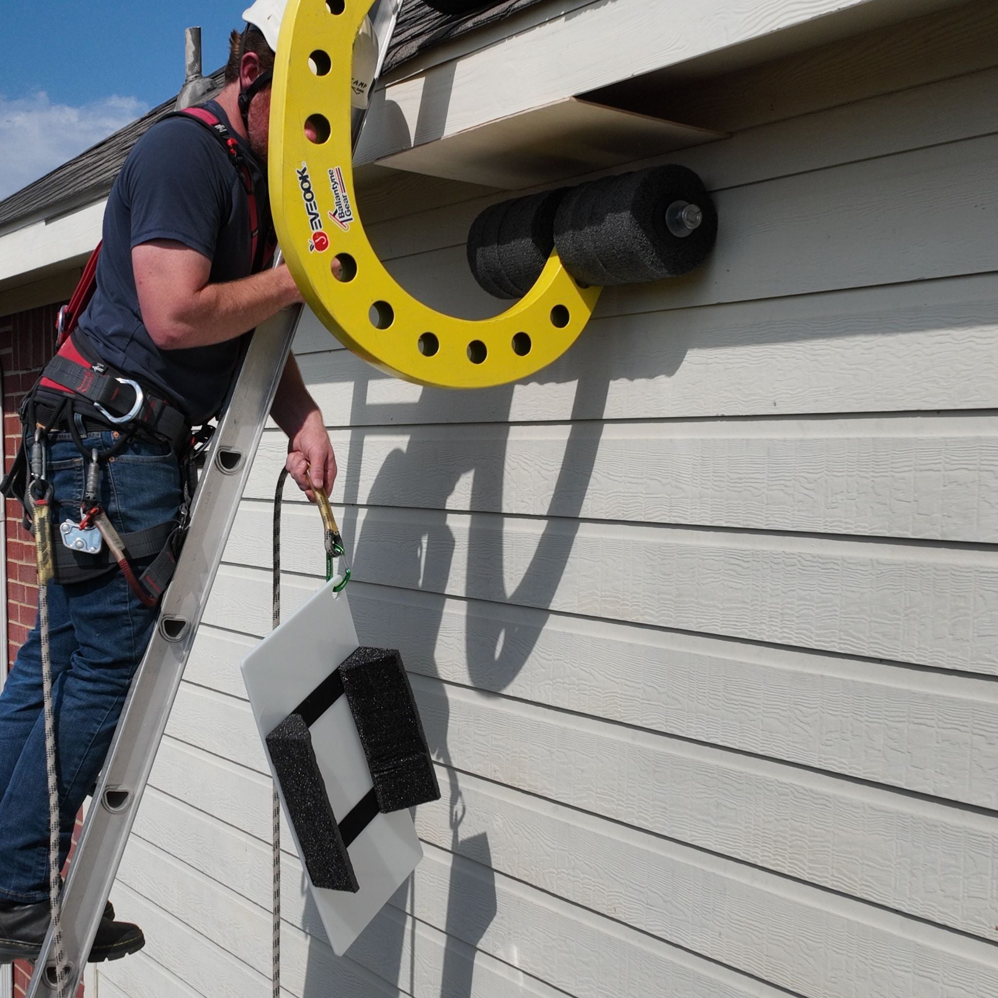 Roof worker on a ladder wearing PPE raising up SoffitGuards to protect vulnerable soffits when using the Eveook Fall Protection System