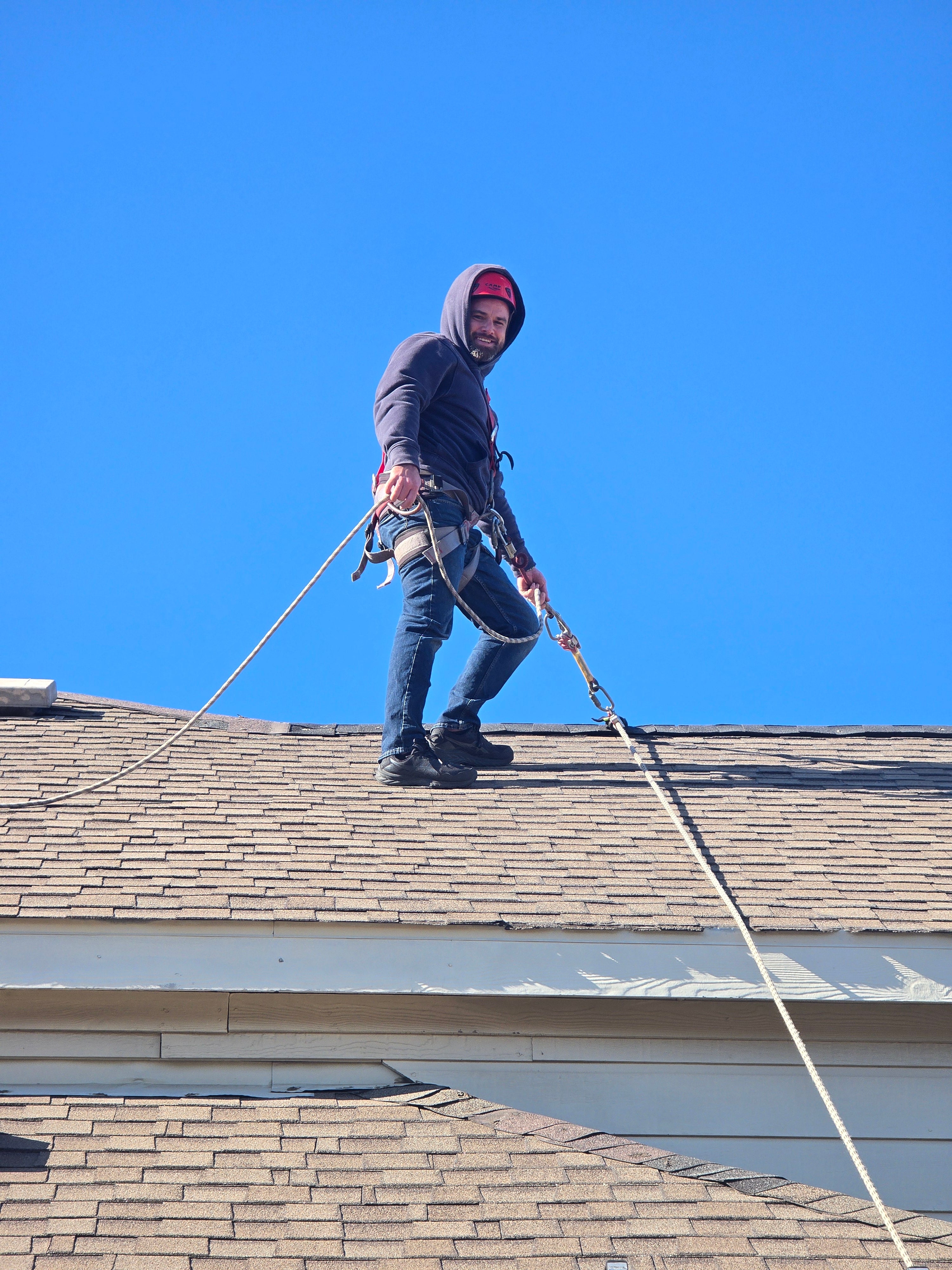 Worker using the Eveook fall protection roof anchor system on sloped roof with asphalt shingles
