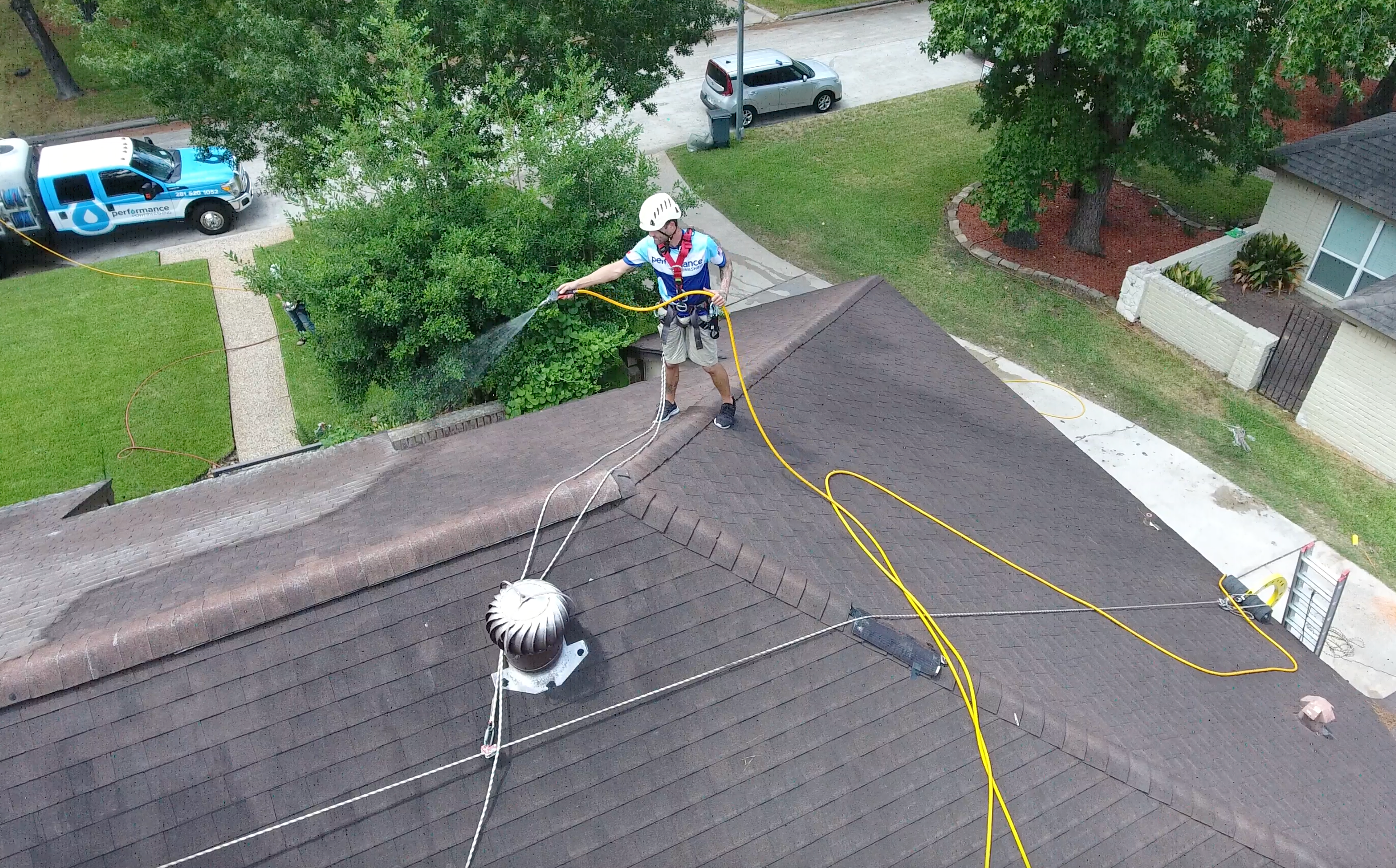 Roof cleaning worker on a roof peak spraying the roof while using a roof safety harness and anchorline system for fall protection on residential roof